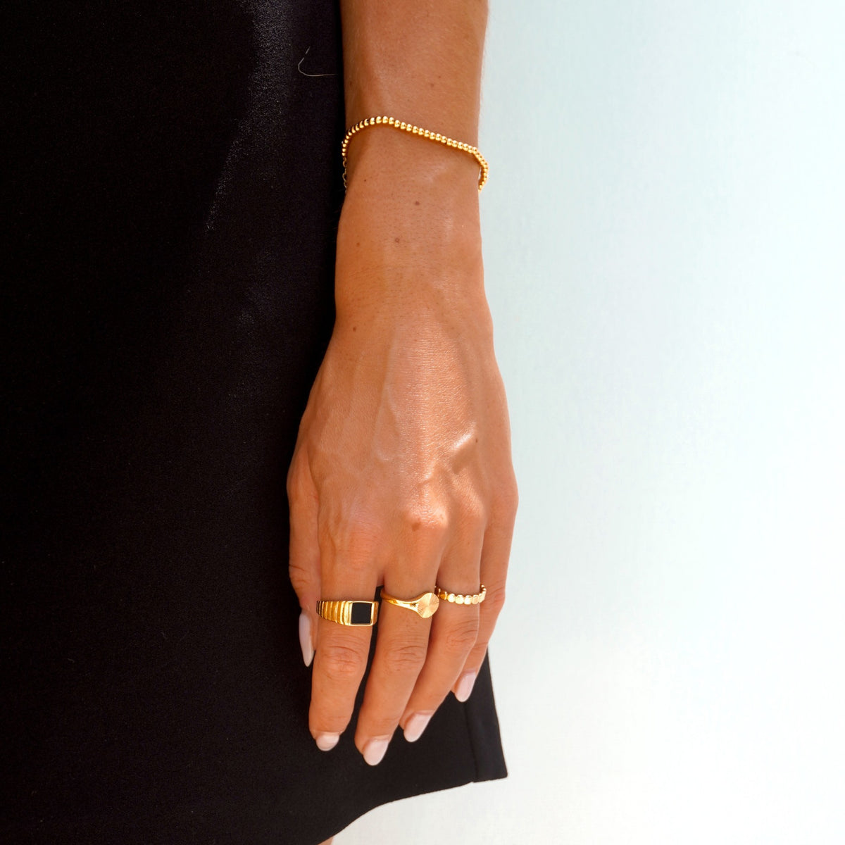 Black onyx signet ring stacked with gold rings and a gold beaded bracelet